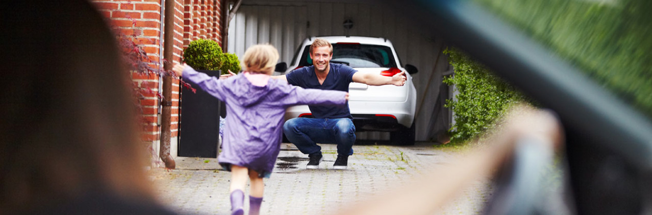 A young daughter running to her father in front of their garage