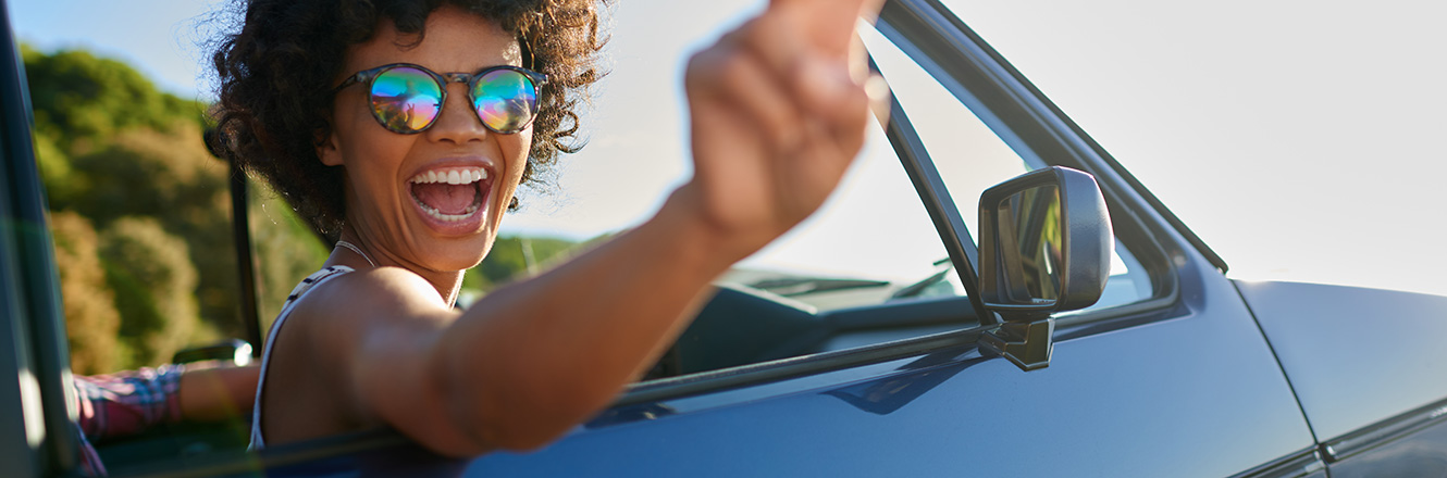 Woman in sunglasses smiling and putting up a peace sign in the passenger seat of a convertible car