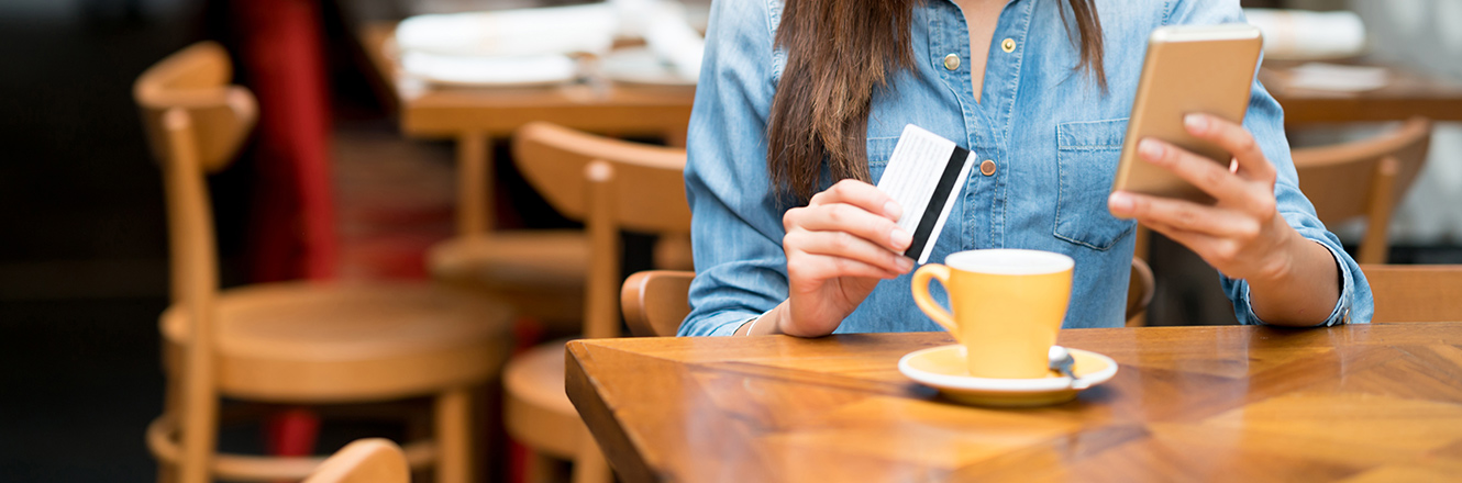 woman using phone and card in cafe with tea cup