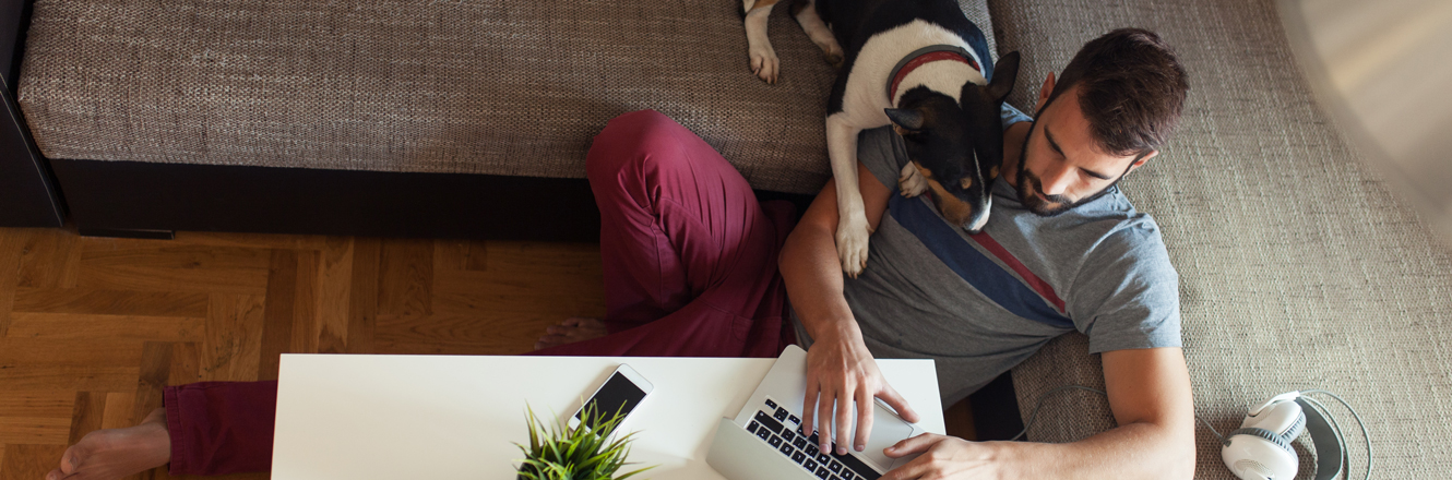 man at home banking on laptop with his dog laying on his shoulder
